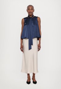 Navy satin sleeveless top with a tie neck, paired with a cream midi skirt. Smooth texture and flowing design, finished with black pointed flats.