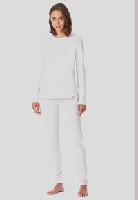 Top bianco a maniche lunghe e pantaloni abbinati in un morbido tessuto testurizzato. Vestibilità comoda con polsini a costine e un piccolo logo sul bordo.
