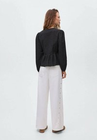 Crna, teksturirana bluzica s puf rukavima i peplum rubom u kombinaciji s bijelim širokim hlačama s bočnim gumbima.