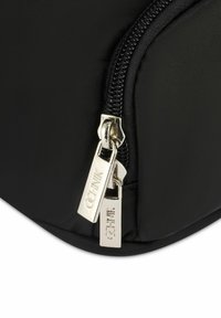 Czarna nylonowa torba o gładkiej fakturze, z zamkiem błyskawicznym w kolorze srebrnym z dwoma uchwytami oraz z logo wygrawerowanym na etykietach zamka.