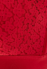Crvena čipka s cvjetnim uzorkom i teksturiranom završnom obradom, s glatkim donjim dijelom. Materijal ima vidljive detalje šivanja.