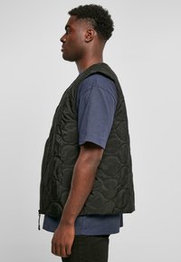 Zwarte gewatteerde vest met een rits aan de voorkant, mouwloos ontwerp en ronde patronen. Draagt over een blauwe shirt, wat een casual stijl laat zien.