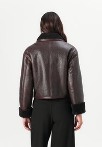 Burgunderfärgad läderjacka med en kortad design, shearling-krage och mjuka detaljer vid ärmarna. Bakvy visar en slät yta och minimal sömnad.