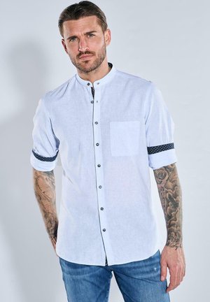 Hellblaues Kurzarmhemd mit Stehkragen, schwarzen Knöpfen, Tasche und gemusterten Manschetten. Aus einem strukturierten Stoff gefertigt.