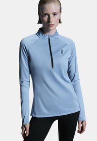 Himmelblaues langärmliges Quarter-Zip-Oberteil aus strukturiertem Stoff, mit schwarzem Zipper und Logo auf der linken Brust. Designed für Fitness.