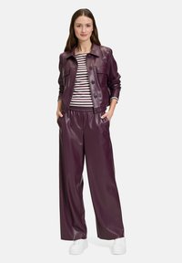 Burgundowa kurtka z sztucznej skóry z dwoma przednimi kieszeniami, zestawiona z dopasowanymi spodniami w szerokim kroju i paskowaną koszulą. Całość uzupełniają białe trampki.