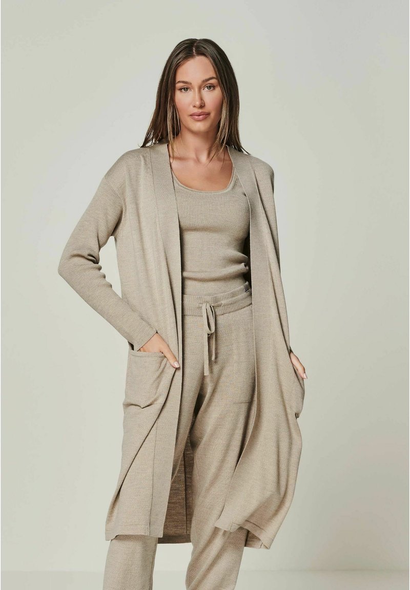 Beige Cardigan mit langen Ärmeln und Taschen, getragen über einem passenden gerippten Tanktop und Jogginghose mit Tunnelzug, das einen weichen, strukturierten Stoff zeigt.