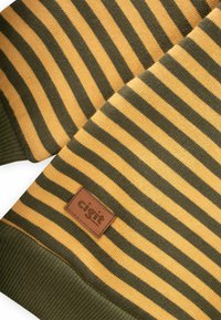 Svītrainā džemperī dzeltenā un tumši zaļā krāsā ir teksturēta adījuma, ribotas apkaklītes un brūna ādas birka ar "cigit" zīmolu.