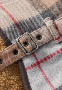 Close-up of a beige and gray plaid fabric belt with black eyelets and a metal buckle engraved with "Barbour."