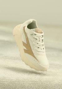 Adidași albi cu accente bej deschis, materiale din plasă și piele suferință, vârf rotund, sistem de prindere cu șireturi și talpă texturată. Numele brandului "HI-TEC" vizibil.