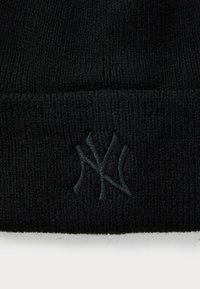 Svart strikket beanie med en mørk brodert "NY"-logo på forsiden, som viser en teksturert stoffdetalj.
