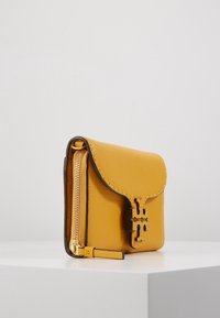 Cartera de cuero texturizado amarillo con tapa, herrajes dorados y un zipper lateral. Presenta un logotipo en relieve y bordes oscuros contrastantes.