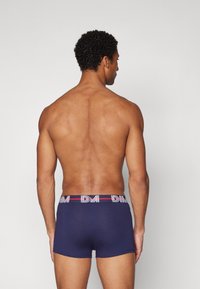 Marinefarbene Boxer-Briefs aus weichem Stoff mit einem breiten Bund, der ein logo in rot-weißen Streifen zeigt. Glatte Textur, körpernahe Passform.