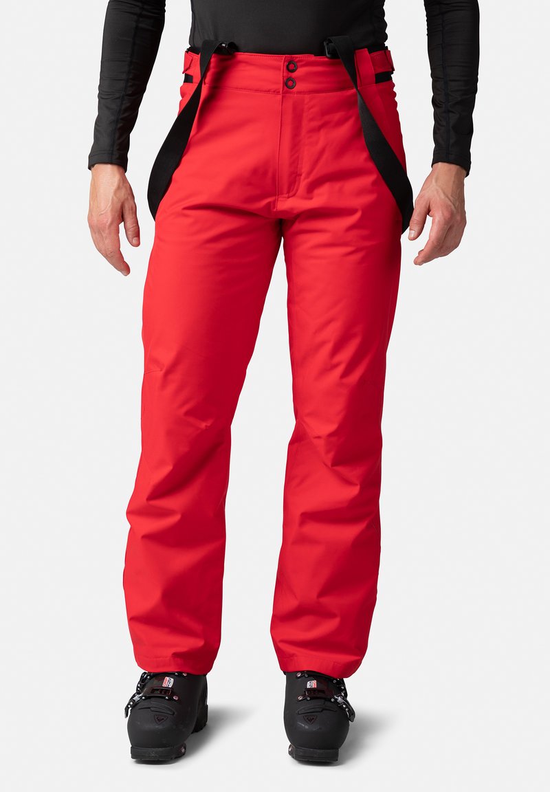 Röda skidbyxor gjorda av vattentåligt material, med justerbara remmar, två framknappar och rak benmodell.
