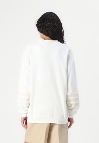 Sweatshirt branco com mangas longas, punhos canelados e decote redondo; apresenta três riscas horizontais em cada manga, textura suave.