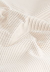 Tessuto morbido bianco sporco con una sottile texture a coste verticali e pieghe delicate.