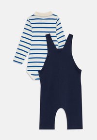 Wit babybodystocking met lange mouwen, blauwe strepen en een beige kraag, gecombineerd met een effen donkerblauwe mouwloze romperbroek.