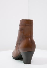 Bota de tobillo de cuero marrón con un diseño curvado, puntera redonda y un leve tacón. Presenta acentos de costura y una textura suave.
