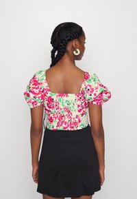 Top de flores com mangas bufantes, apresentando um padrão em verde pastel, rosa e branco. Saia preta completa o conjunto.