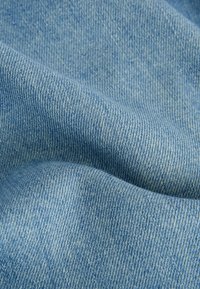 Denim stof in lichtblauw, met een gladde textuur en een diagonale weefpatroon. Licht gekreukt, wat de flexibiliteit en zachtheid benadrukt.