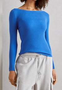 Ribbed long-sleeve top in bright blue, featuring a wide boat neckline and a fitted silhouette, paired with light grey drawstring sweatpants.