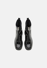 Botines de charol negro con cierre de cremallera, punta redondeada, paneles laterales texturizados y suela de goma baja.