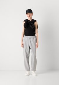 Zwarte mouwloze top, grijze joggingbroek met elastische tailleband, zwarte pet en witte sneakers. Glad textuur en casual ontwerp.