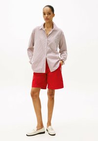 Chemise rayée blanche et rouge, associée à un short rouge. La tenue est complétée par des mocassins blancs avec des accents dorés.