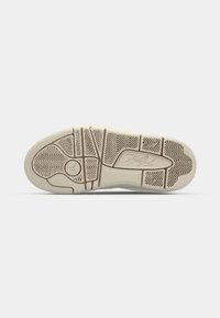 Semelle de chaussure avec une bande de roulement en caoutchouc beige comportant un logo Jumpman près du talon et une gravure signature près de la zone de la voûte plantaire.