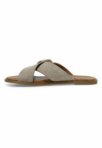 Chanclas de ante en gris claro con tiras cruzadas y un acento dorado redondo. Suela plana con un interior marrón suave. Diseño minimalista.