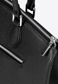 Zwarte lederen handtas met textuur, voorzien van zilverkleurige hardware, een bovenrits met contrasterende witte stiksels en een voorzak met rits.