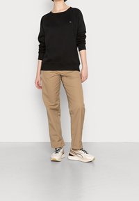 Felpa nera con colletto tondo e polsini a costine, abbinata a pantaloni beige a gamba dritta e sneakers bianche con dettagli neri.