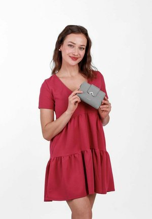 Pink cotton dress with a flared hem, worn by a person holding a small gray wallet with a flap and embossed detail. Clear white background.