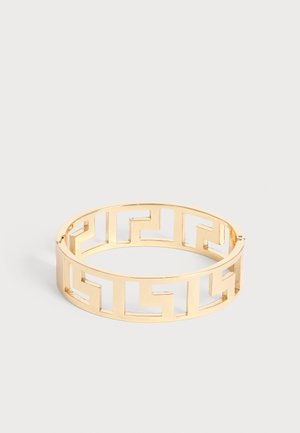 Bracciale metallico dorato con un design a motivo labirinto geometrico aperto, mostrato su uno sfondo chiaro e uniforme.
