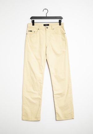 Pantalones de algodón beige de pierna recta en un perchero negro. Cuentan con cinco bolsillos, herrajes metálicos y una textura sutil. Sin patrones visibles.