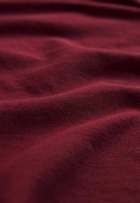 Primo piano di un tessuto bordeaux spiegazzato che mostra una fine texture e un motivo a maglia.
