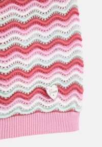 Knitted top in wavy patterns of red, pink, and mint with a heart-shaped silver tag displaying the brand "Guess." Pink ribbed hem.