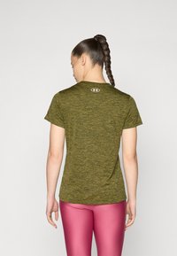 Kortermet grønn heathered treningstrøye med rund hals og logo på ryggen, kombinert med glansfulle rosa leggings.