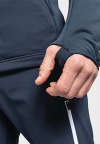 Navy athletic top with textured fabric feature and thumbhole cuffs paired with solid navy pants, showcasing a zippered pocket in white.