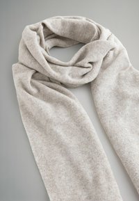 Lys beige tørklæde lavet af blødt, tekstureret stof, hængende i en løkke. Har en glat overflade med subtile farvevariationer.