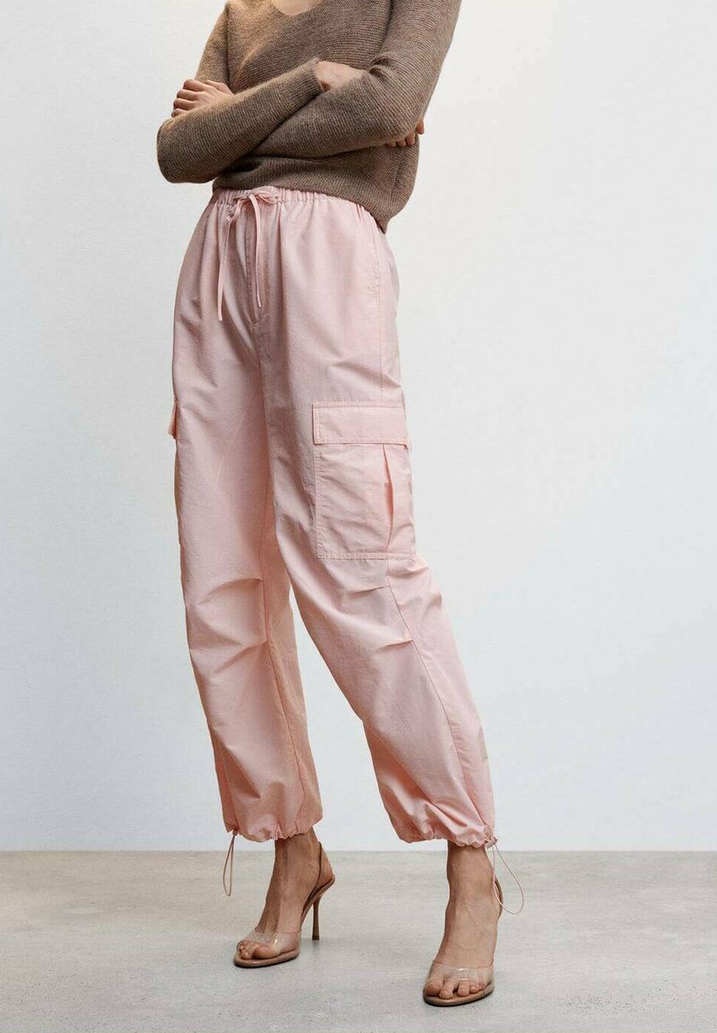 Pantalones cargo rosa claro con puños ajustables, que presentan dos bolsillos laterales y un ajuste relajado. Combinados con tacones transparentes y con tiras.