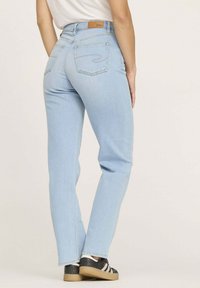 Jean en denim bleu clair à coupe droite, avec deux poches arrières et une étiquette en cuir marron au niveau de la taille.