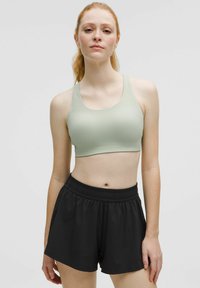 Crop top atlético de color verde claro con escote redondo, combinado con pantalones cortos atléticos de cintura elástica en negro, ambos fabricados con una tela suave y elástica.