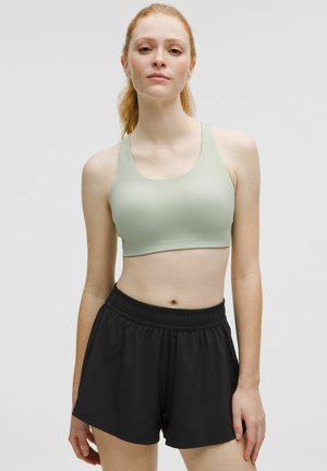 Világoszöld sport crop top, kerek nyakkivágással, fekete, elasztikus derékú sportnadrággal párosítva, mindkettő sima, rugalmas anyagból készült.