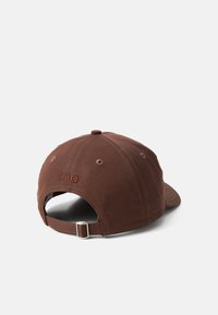 Boné de algodão castanho com uma aba curva, apresentando o logótipo bordado "tho" na parte de trás e uma fivela de metal ajustável na alça.