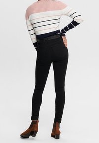 Jean skinny noir taille haute avec deux poches arrière, assorti à un pull côtelé multicolore avec des rayures roses, blanches et bleu marine.