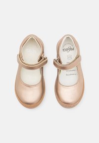 Zapatos de cuero bronce con punta redondeada, correa ajustable y suela de goma texturizada marrón, que cuentan con una plantilla acolchada.