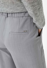 Lichtgrijze op maat gemaakte broek met een gladde textuur, voorzien van een achterzak en een klein metalen accentlabel.