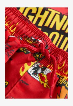 Czerwone kąpielówki z wiązanym paskiem w talii, charakteryzujące się błyszczącym wykończeniem i wielokolorowymi grafikami płomieni oraz postaci z kreskówek.