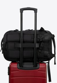 Valigia rigida rossa con superficie testurizzata, sormontata da una borsa morbida nera fissata con cinghie, dotata di due maniglie nere estensibili.